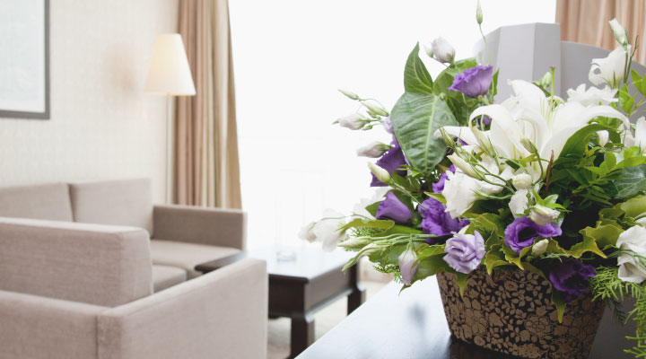 Ein warmes lichtdurchflutetes Hotelzimmer. auf der Komode steht ein Gesteck mit weien und violettesn Rosen